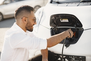Jeune homme rechargeant sa voiture électrique, symbole de l’électromobilité urbaine et durable.